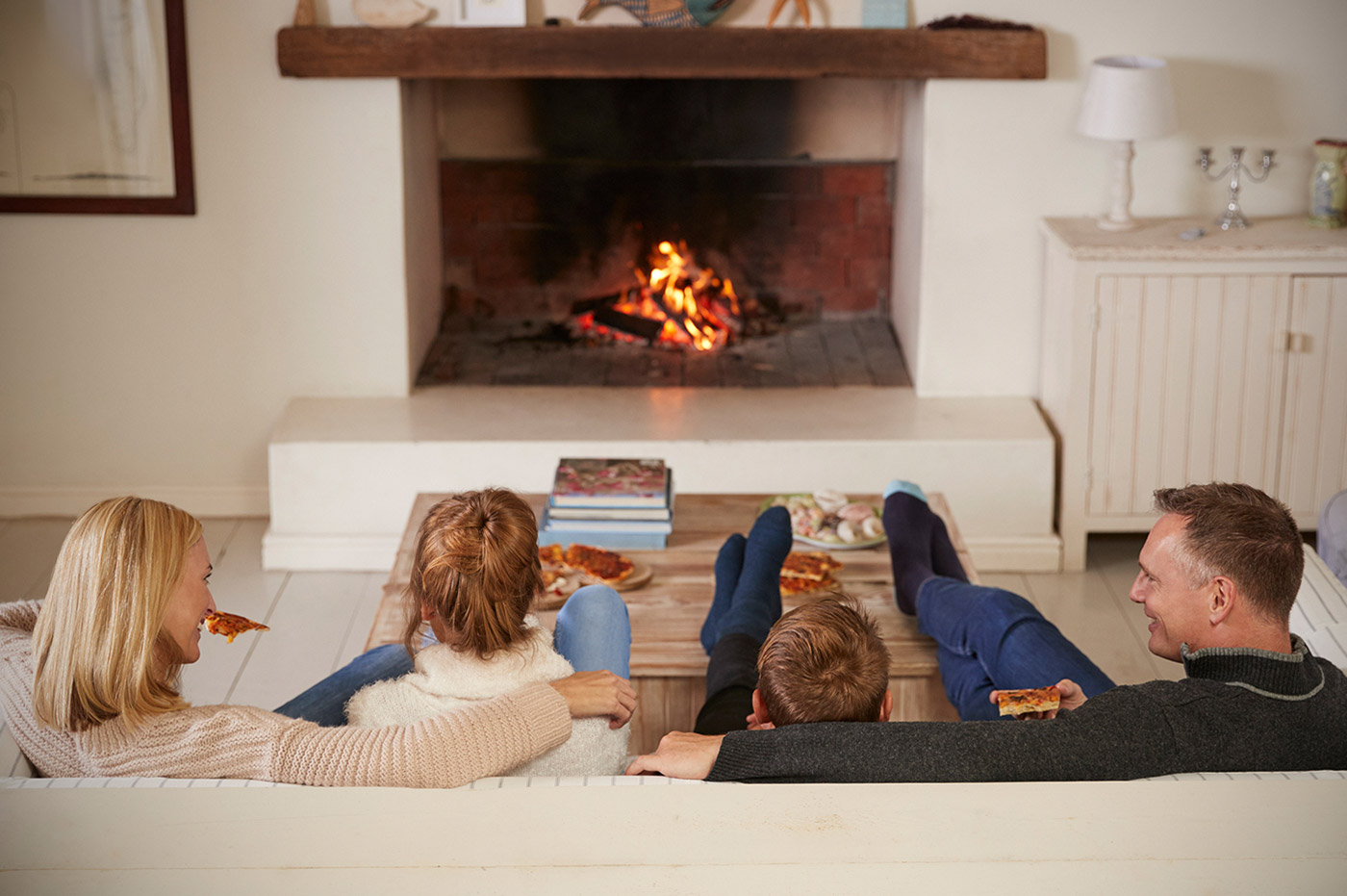 A family sitting together on the couch in front of a lit fireplace.